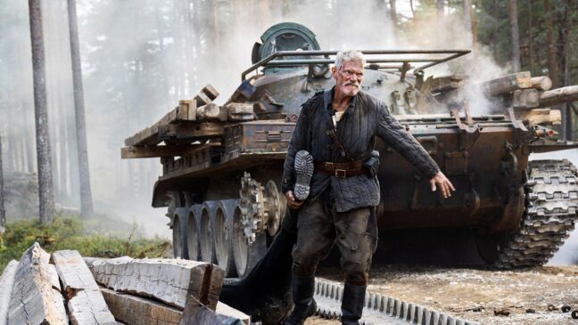 Stephen Lang drar någon i benet, bakom honom syns en stridsvagn.