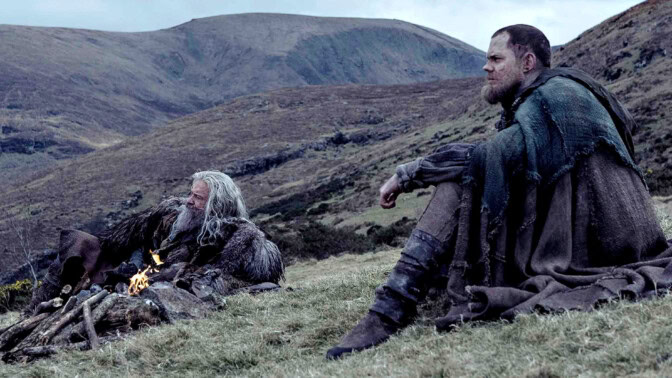 Hugh Jackman som Robin Hood och Bill Skarsgård som Lille John. De chillar i gräset med bergen som bakgrund.